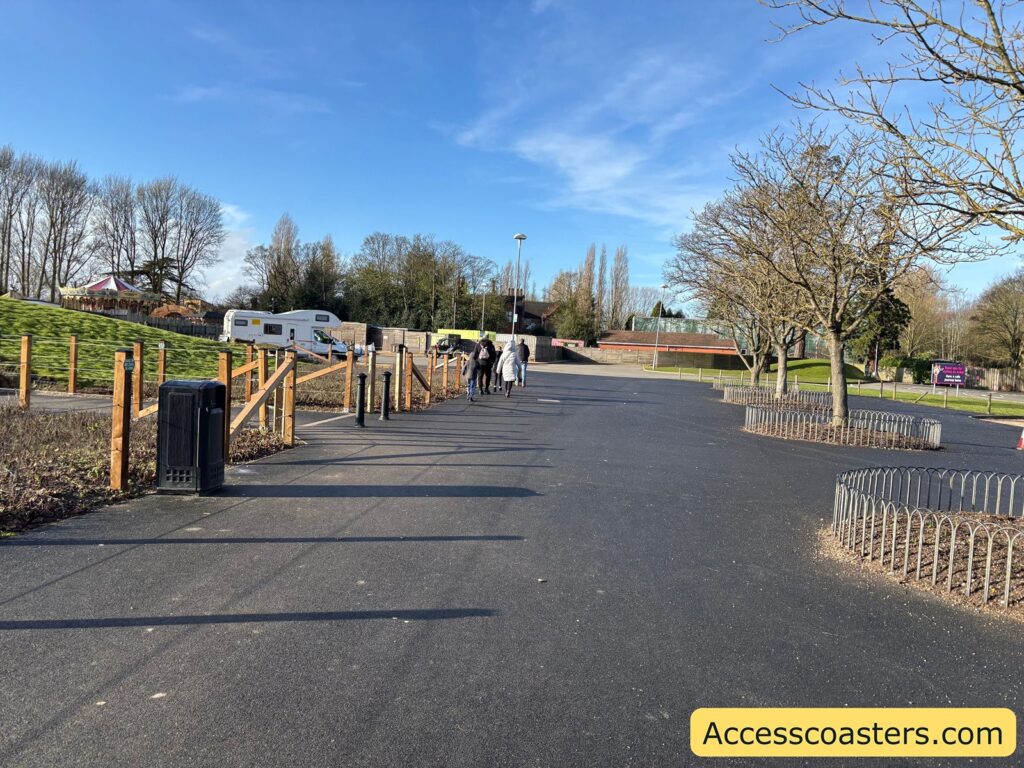 Paved path leading from the car park toward the attraction entrance, with railings and trees along the route.
