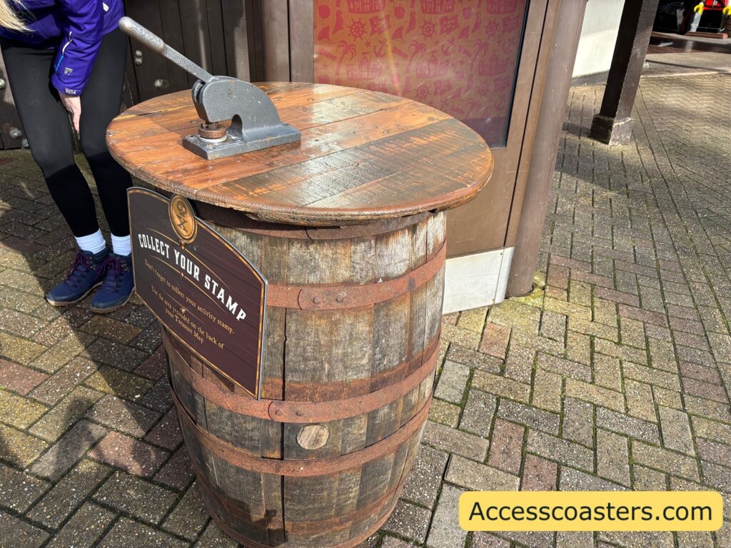 A wooden barrel set up as a stamp station, with a large metal stamp mounted on the top and a sign on the front indicating it’s for collecting a stamp.