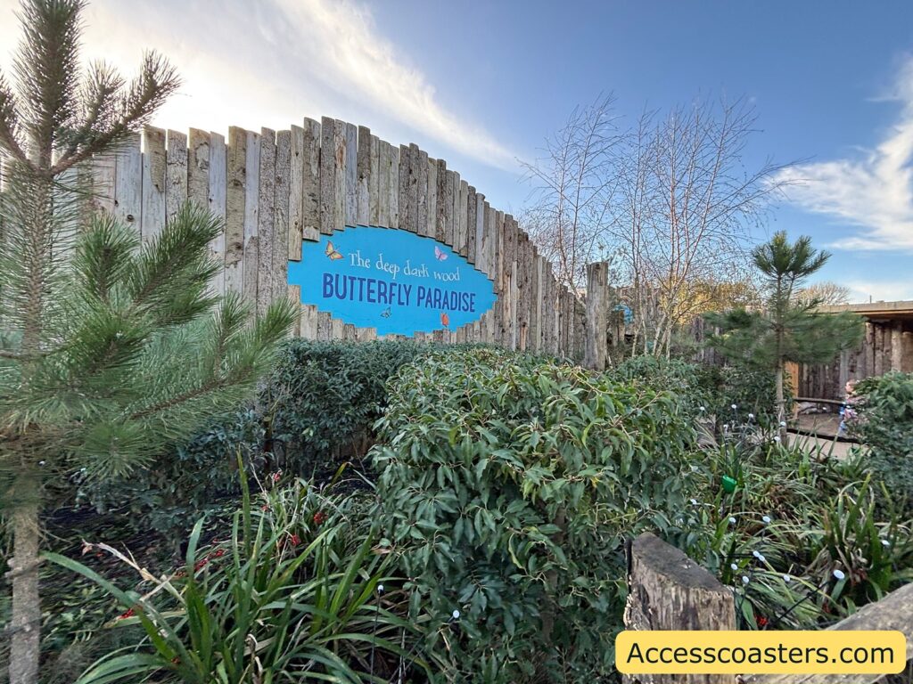 Curved wooden fence with a large blue “Butterfly Paradise” sign above thick planting.
