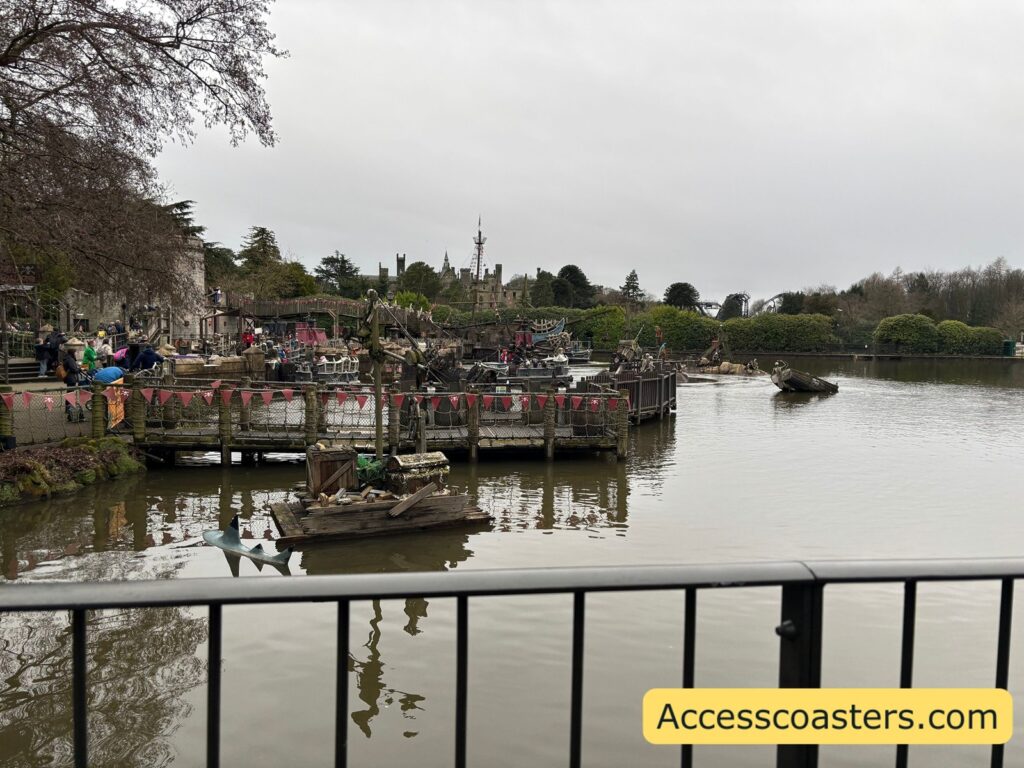 A wide, overcast view across a lagoon with floating docks and small boats; people and actors are gathered near the boats as part of a pirate takeover overlay.