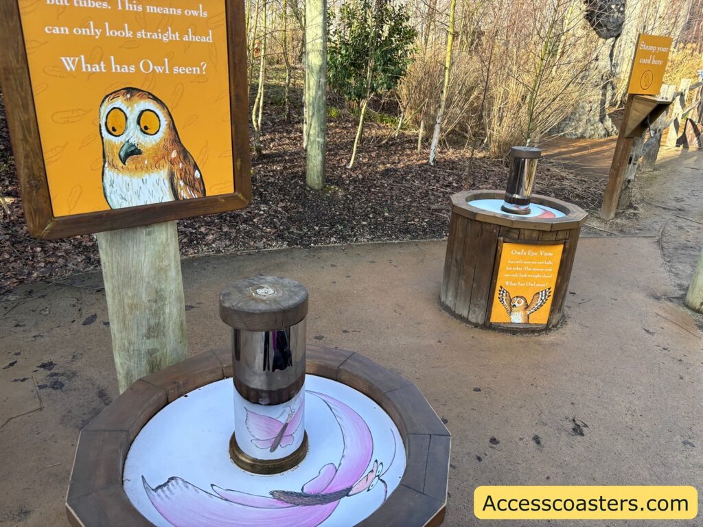 Close-up of an Owl activity sign and a round hands-on station in the foreground, part of the trail’s learning activities.