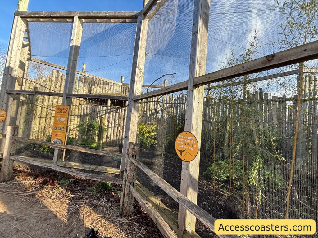 utdoor owl enclosure area with tall netting and wooden supports, with an orange sign attached to the fencing.