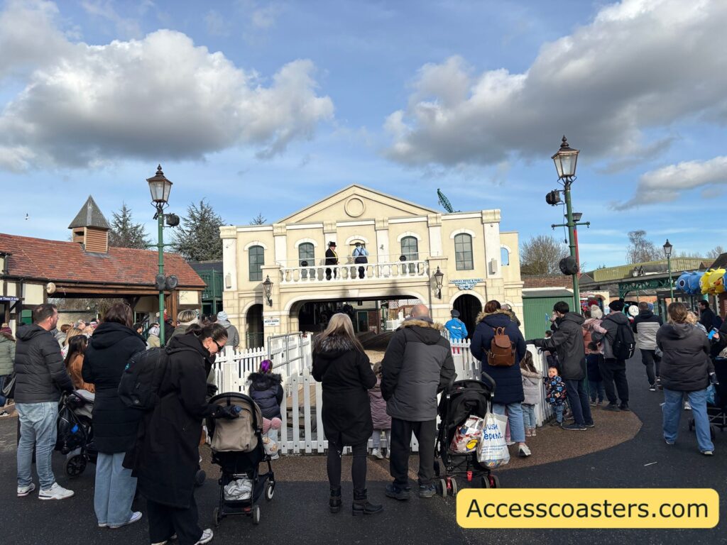 Visitors gather in a crowd with strollers near a white picket fence, watching the Thomas Land entrance building