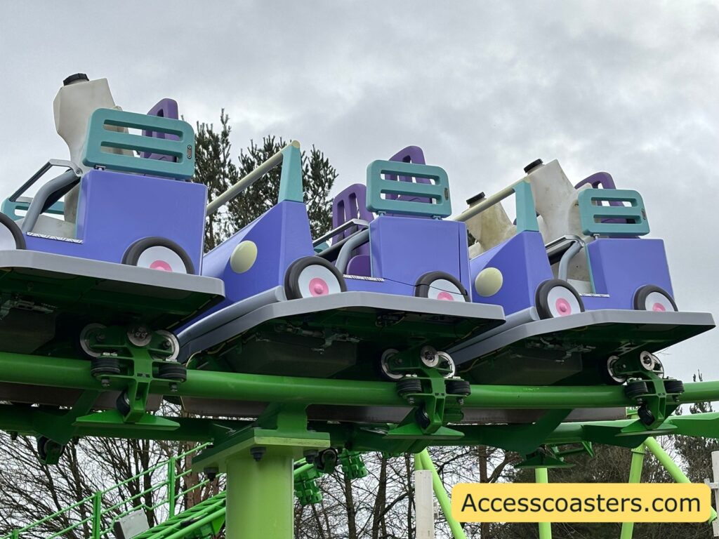a close up of the ride train the ride carts are purple with teal there is a lap bar restraint and test dummies.