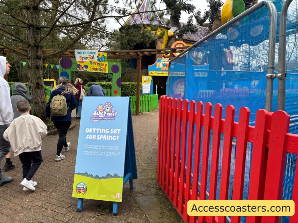 A paved walkway with several people walking. A freestanding sign in the foreground has a blue top and green bottom and reads “GETTING SET FOR SPINNING!”