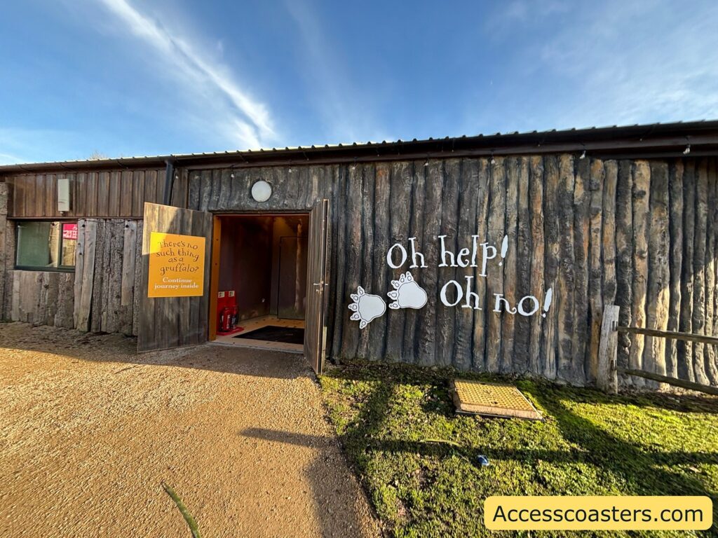 Rustic wooden hut entrance to The Gruffalo area, with “Oh help! Oh no!” painted on the wall beside the open door.
