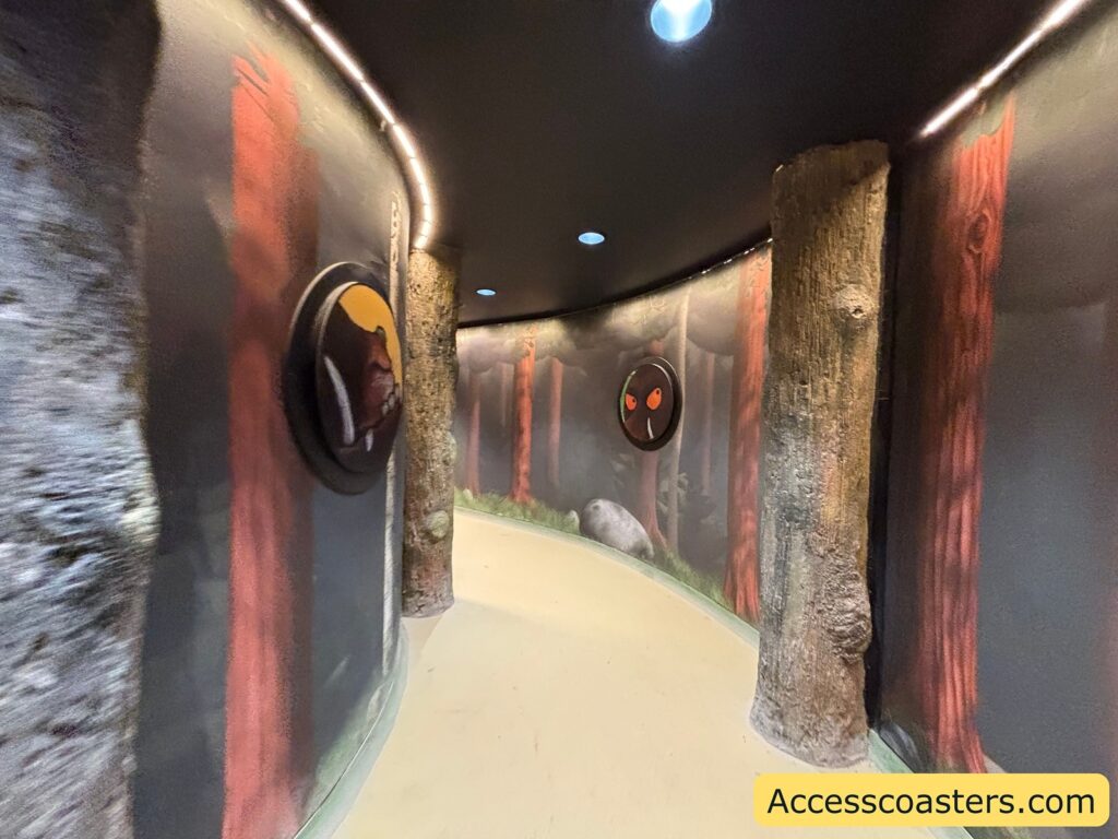 Curved indoor walkway to The Gruffalo, dimly lit with forest-themed walls and log-style pillars.
