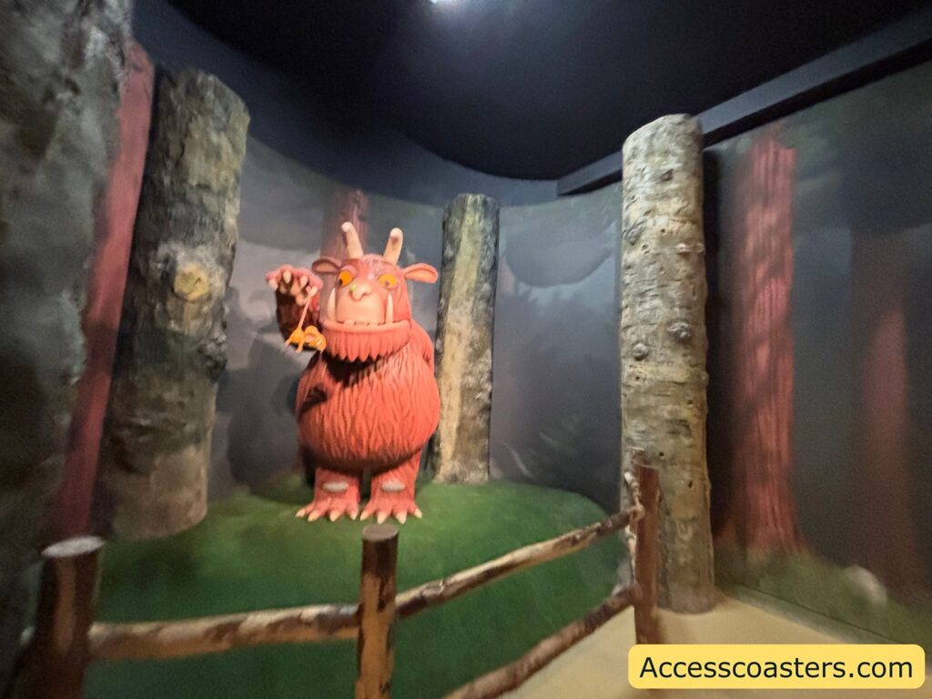 The Gruffalo figure in a dark, forest-themed room, standing behind a low wooden barrier.