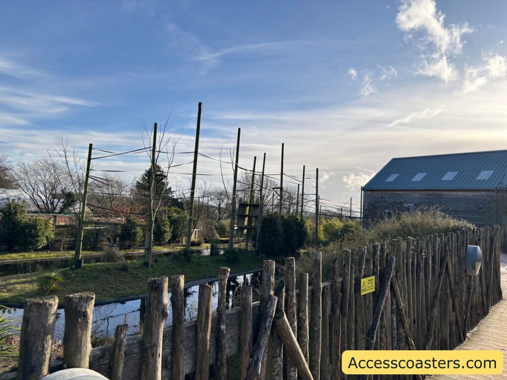 Walkway beside the outdoor gibbon enclosure, with fencing and tall netted poles around a long water channel; no monkeys visible outside.
