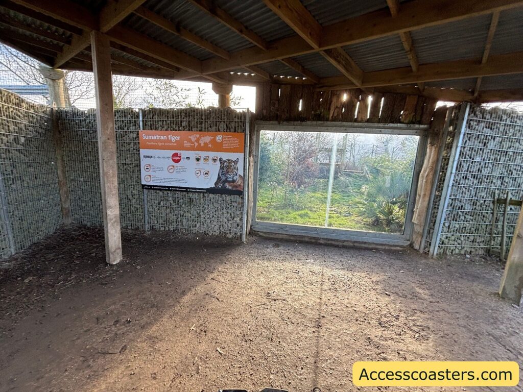 Covered enclosure area with an information sign and and viewing window into the tiger habitat.