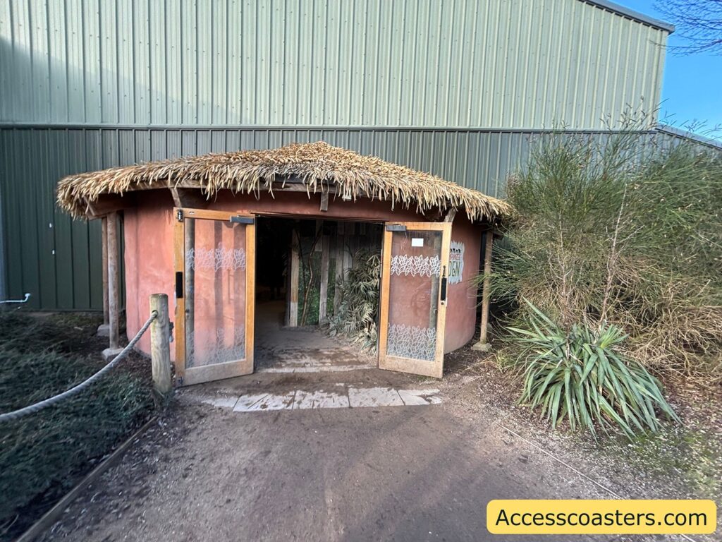  Entrance to Chimpanzee Eden, a small thatched-roof hut leading into the indoor walkthrough area beside the main building.