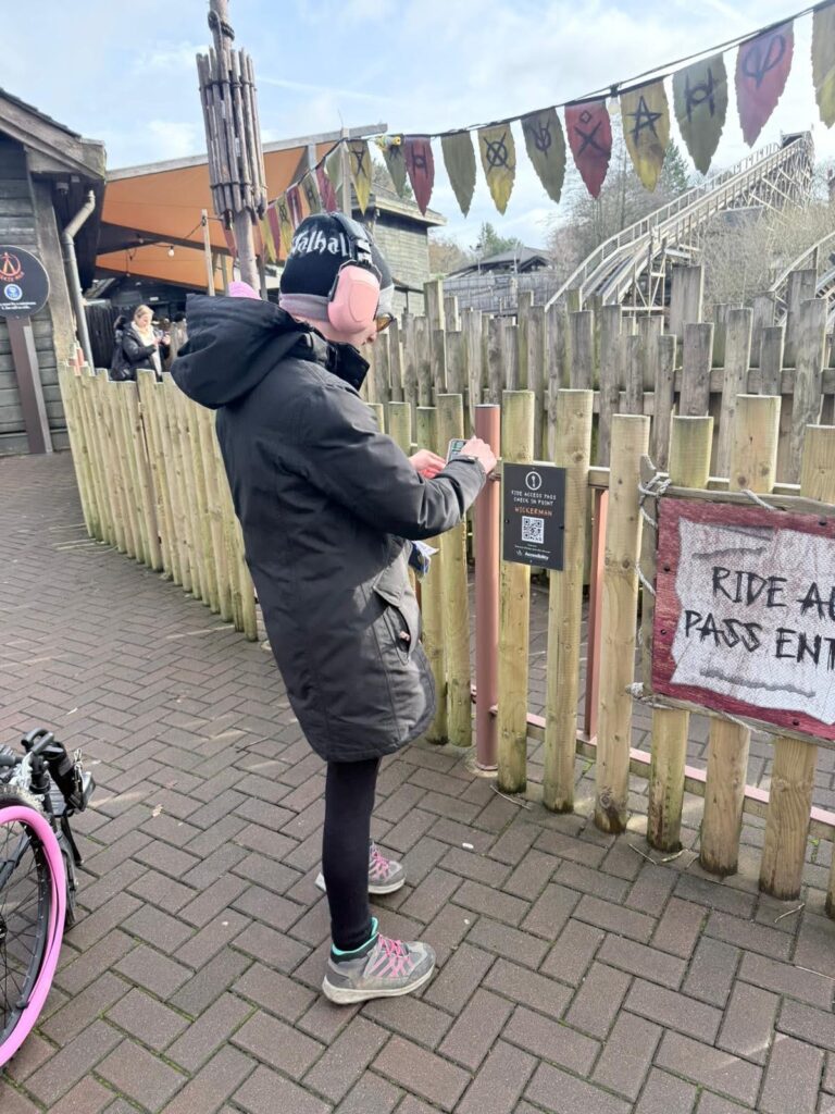 Person in a hooded coat checks in at an outdoor ride access pass entrance beside a wooden fence