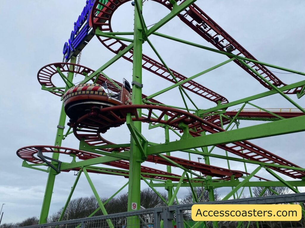 View of the Spinning Coaster track structure from below, showing the bright green supports, red wild‑mouse style track, and a spinning car travelling along a curved section of track.