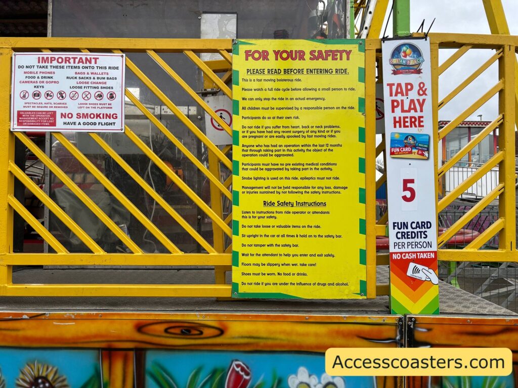 Close-up of the Spinning Coaster safety board  with a large yellow “For Your Safety” sign listing rules and a smaller sign showing the cost of 5 ride credits.