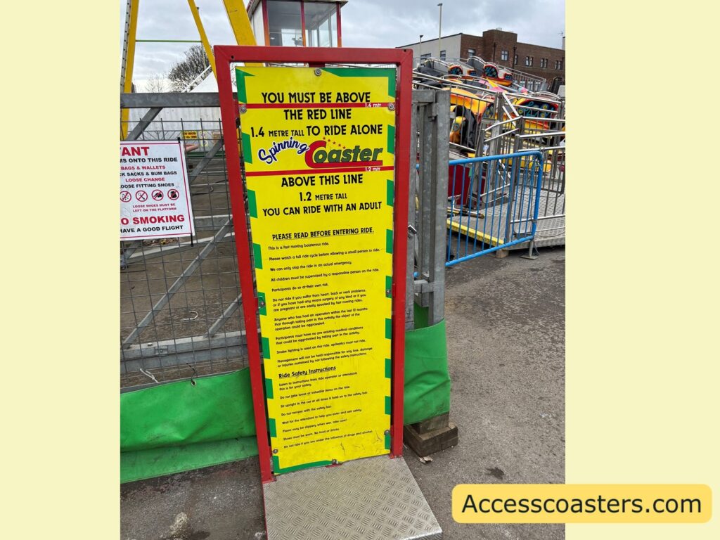 ride information board for the Spinning Coaster beside the entrance, a tall yellow sign with red border listing height restrictions and safety rules