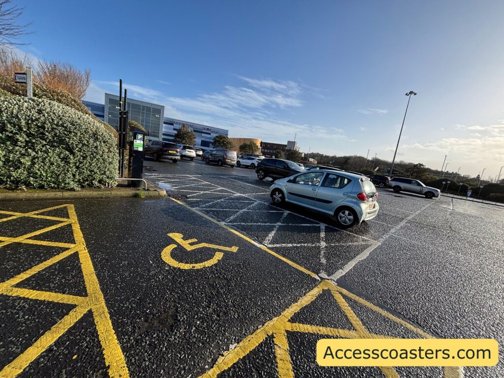 image of blue badge parking space with car park visable in the background. The parkin space has yellow chevrons on both sides and the back of the parking space. 