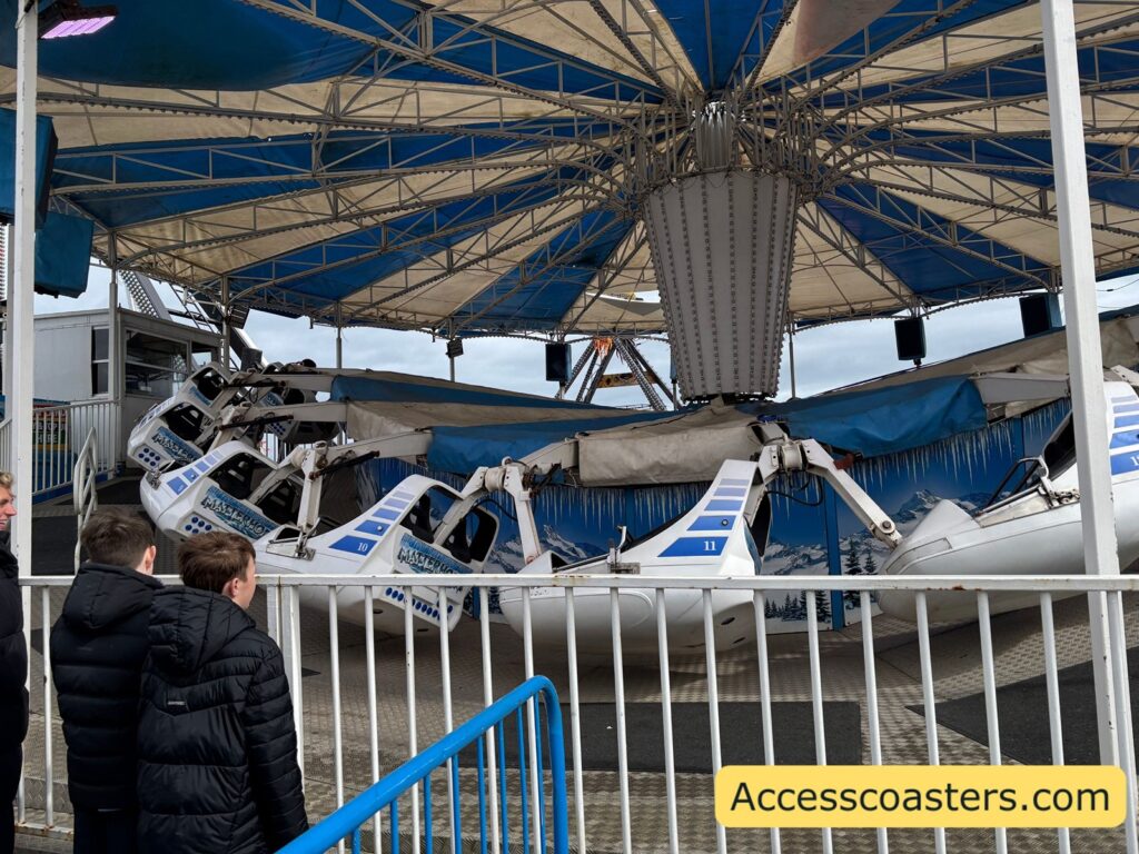 Close-up side view of the Matterhorn amusement ride showing several white and blue swinging cars suspended from a large circular canopy structure