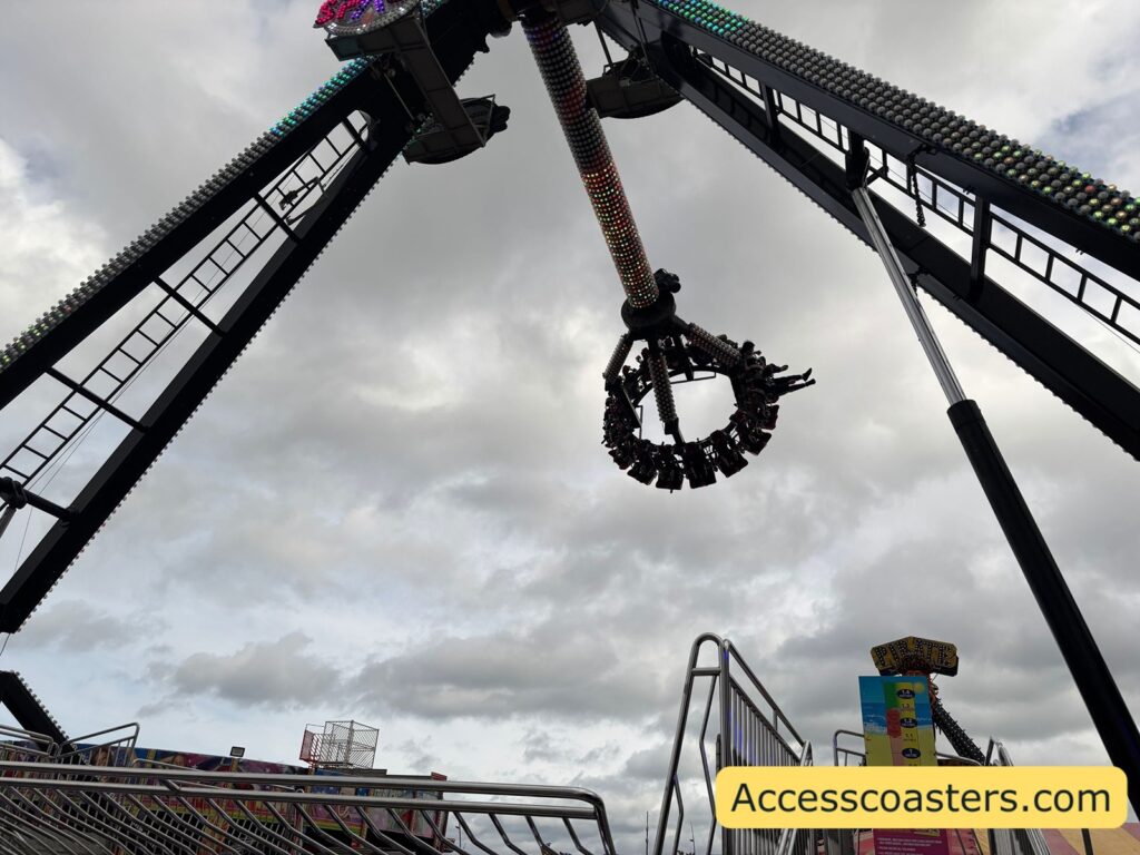 Distant view of the Space ride at full height with its long black arms raised and the circular ring of riders hanging vertically far above the ground