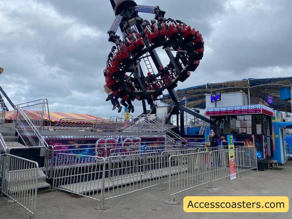 The Space ride in motion with the circular ring of riders tilted and swung high above the platform, riders’ legs hanging outward as the arm lifts them
