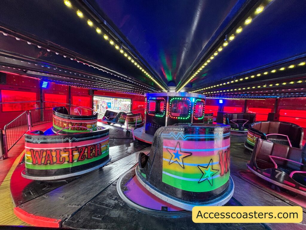 Interior of the waltzer ride during operation, showing multiple rounded spinning cars on a circular sloped platform under a dark ceiling lined with bright rows of colored lights, creating a vivid, fast‑moving atmosphere.