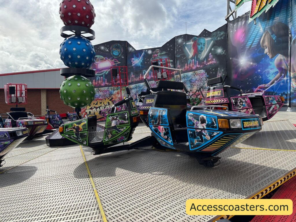 Breakdance funfair ride at Ocean Beach with several brightly decorated spinning cars on a circular platform and a tall central column topped with spherical lights