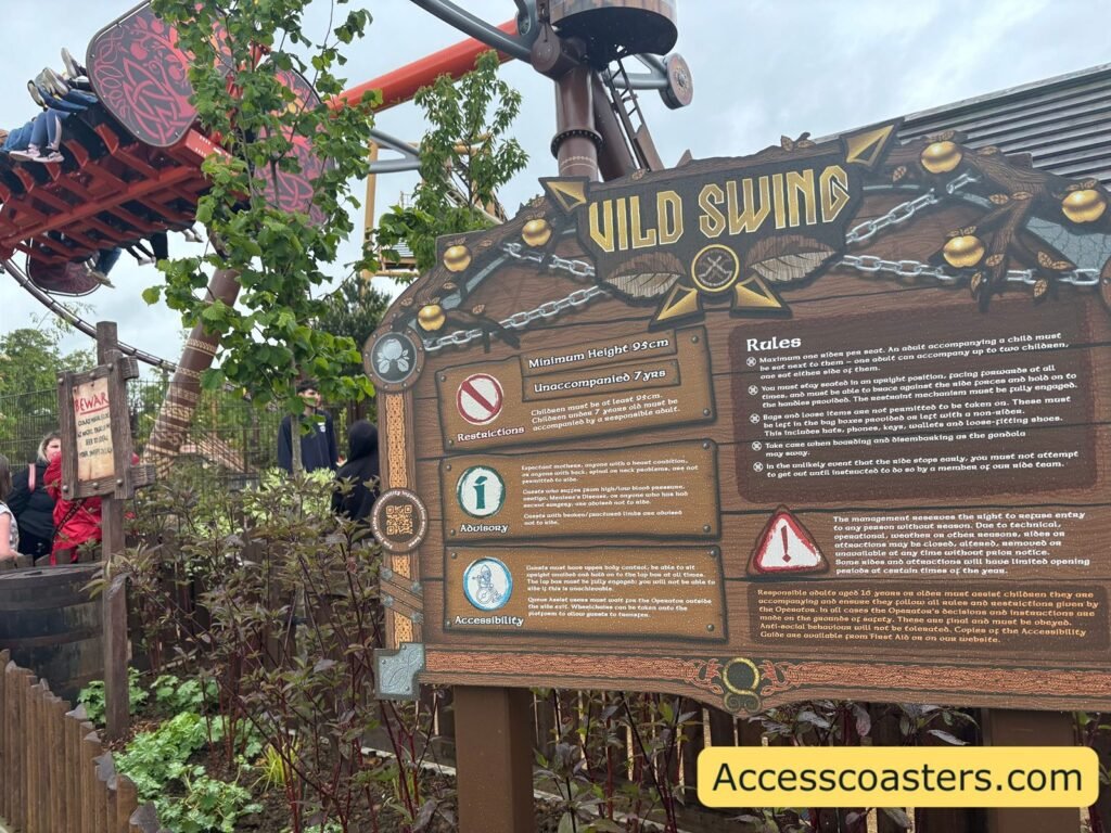 Wooden entrance sign for “Vild Swing” in a themed area, with detailed rider information boards mounted on a rustic fence and part of the colourful swinging ride structure visible behind.

