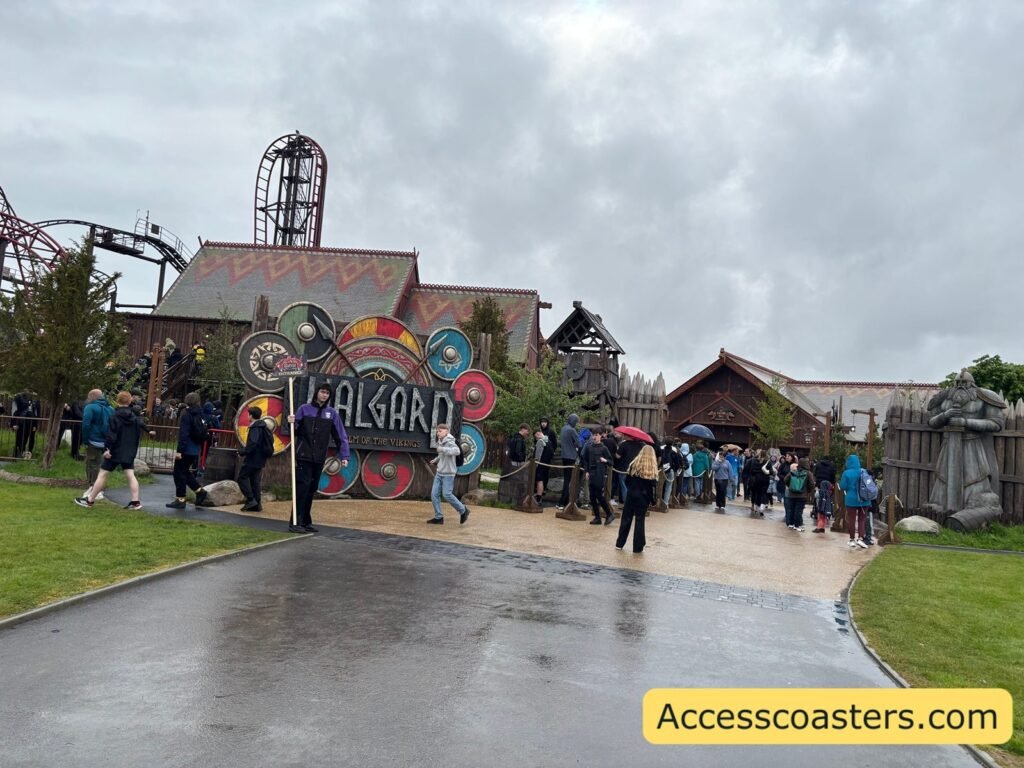 image of entrance to Valgard area you can see wide paths full of people walking and green space eather side you can see viking themed building and drakon vertical drop. 
