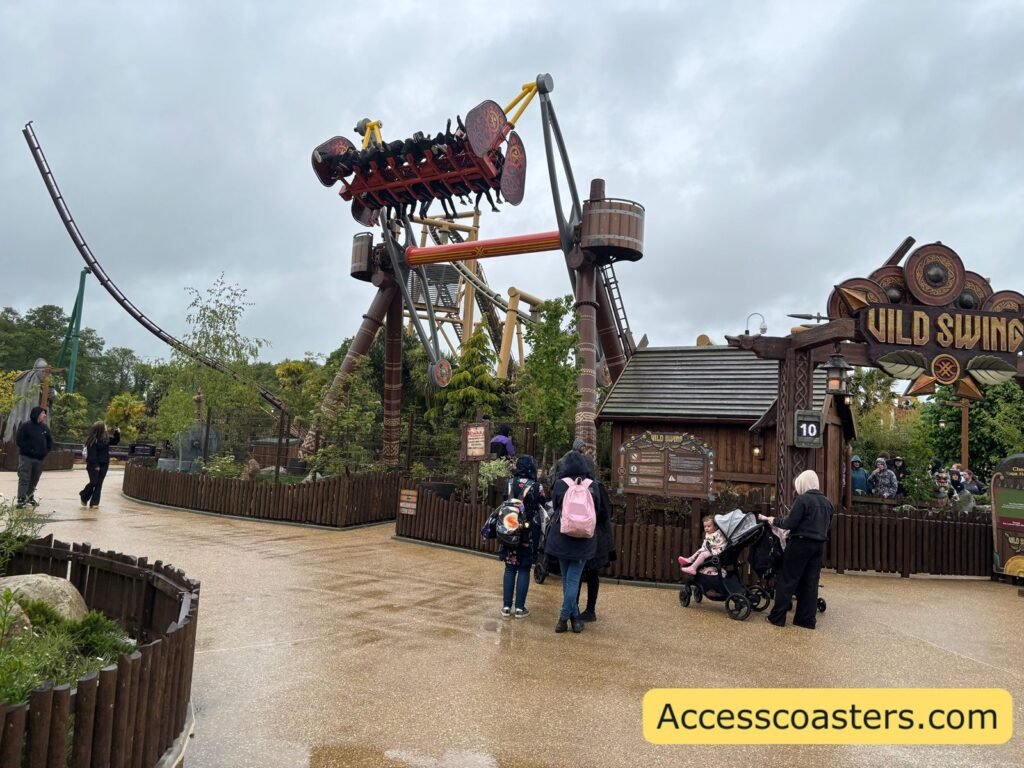Vild Swing mid-swing over the themed landscape, with the wooden ride sign in the foreground, riders elevated on the arm to the right