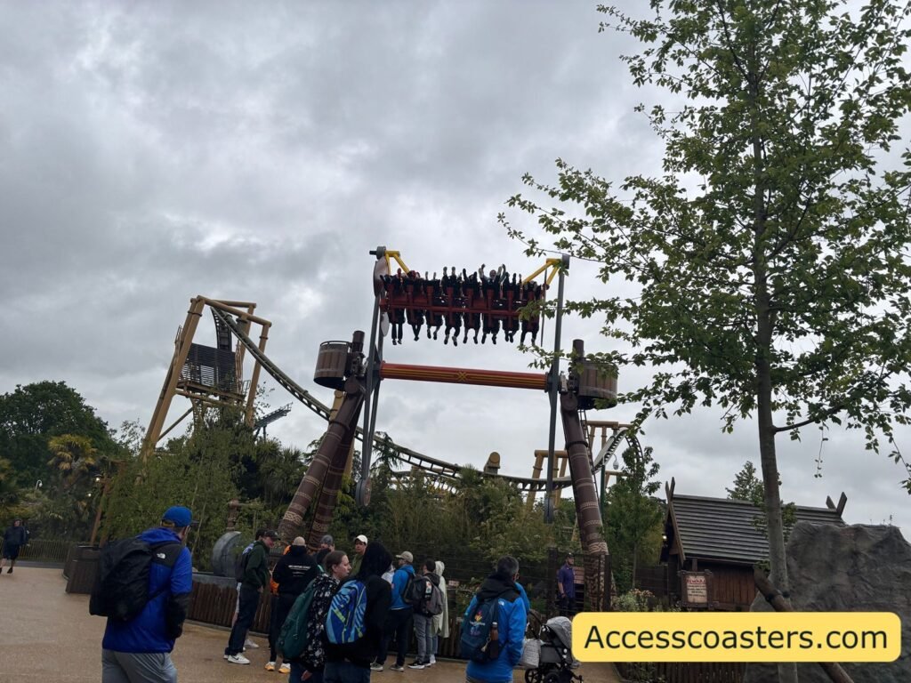 Front view of Vild Swing at the peak of its swing against a cloudy sky, with the gondola full of riders raised high above the ground and onlookers watching from the queue area below.
