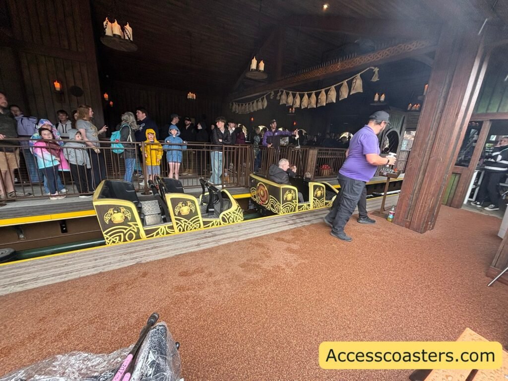 Image of Raven ride station with people waiting behind a fenced queue line and train in the station 