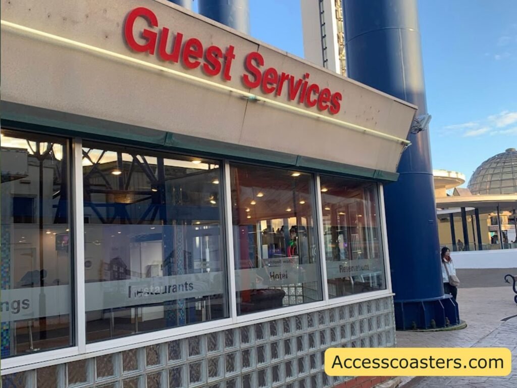 Exterior view of the Blackpool Pleasure Beach Guest Services building, with large windows along the front and a cream‑coloured overhang. Bold red letters reading “Guest Services” run along the top edge.