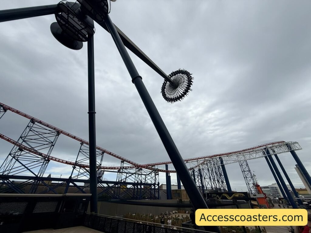Closer angled view of Aviktas’ tall black support arms stretching into a grey overcast sky, with the circular ride gondola hanging at one side and sections of the Big One roller coaster and metal framework visible along the horizon.