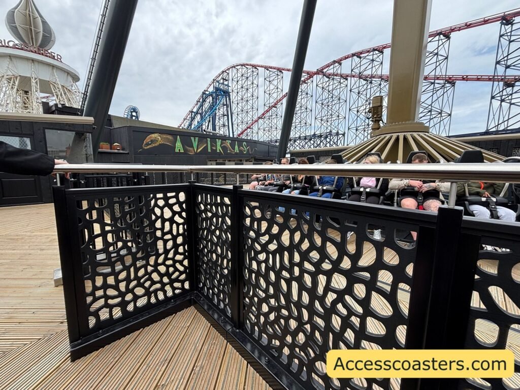 image if view from waiting on the exit ramp the fence and gate into the ride can be seen with people sat on the ride in the station.