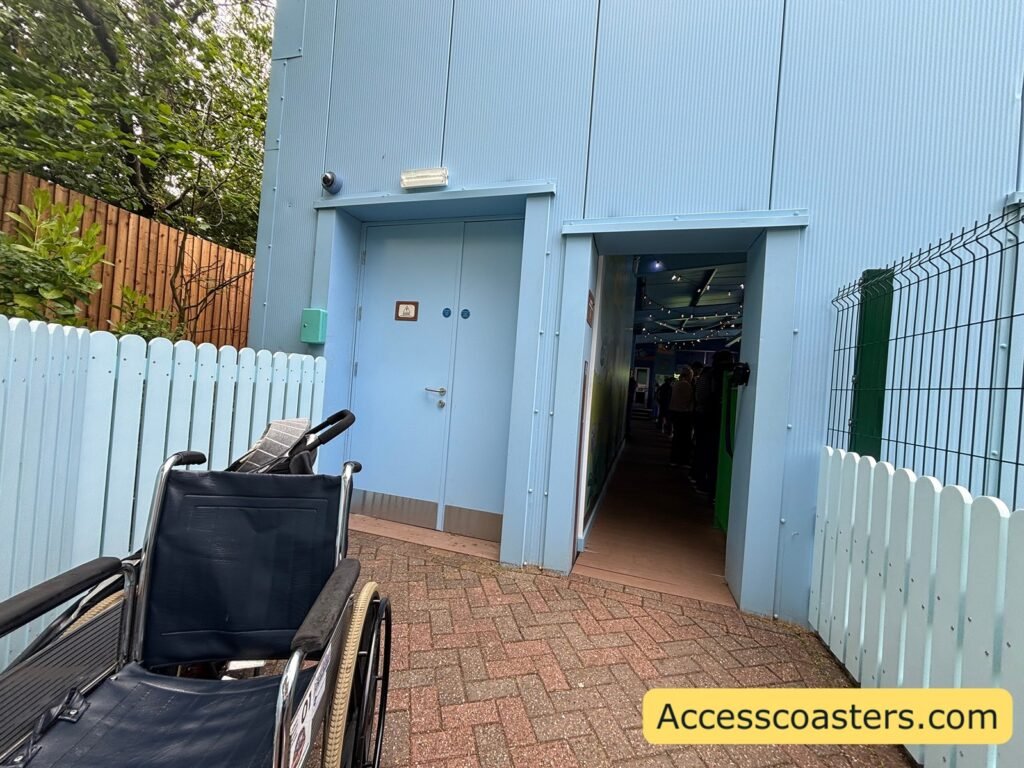 close up of bley wheelchair entrance waiting area a paved ramp is visible with a wheelchair waiting on the path the main focus is the blue ride station building with entrance arch leading into the station