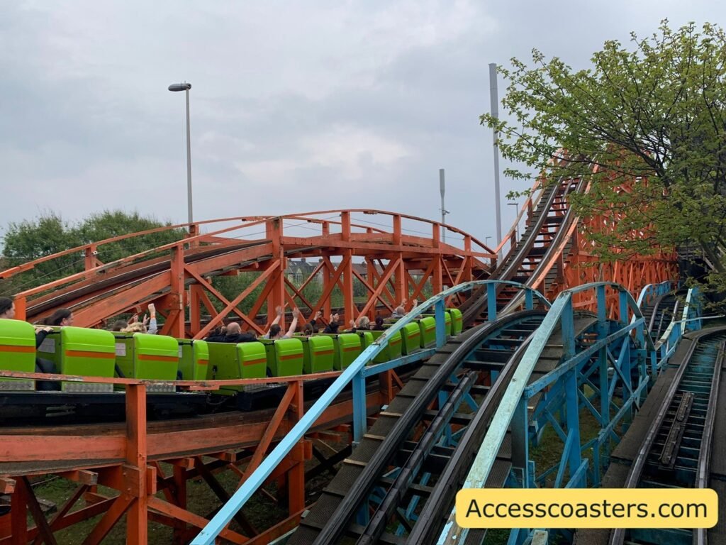 image shows Nickelodeon Streak going up an inclide on the orange wooden track people have got their hands in the air. directly next to the Nickelodeon Streak track you can see a blue wooden track for blue flyer. 