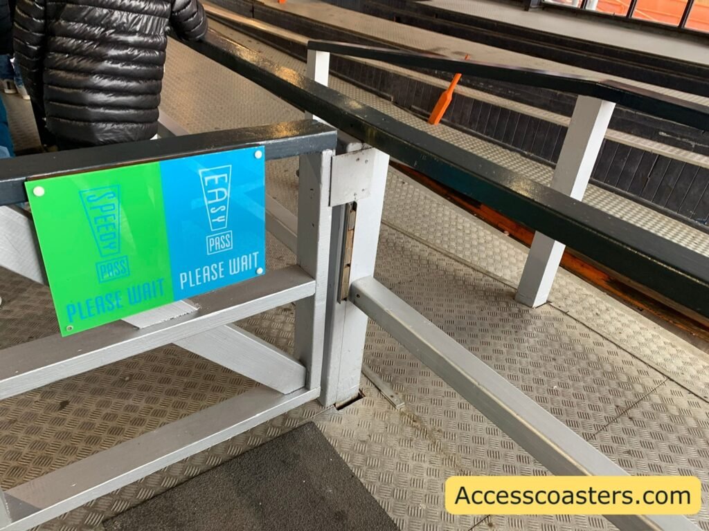 image shoes the front of the easy access pass queue in the ride station with railings and a gate and 2 signs that read easy pass please wait and speedy pass please wait. 