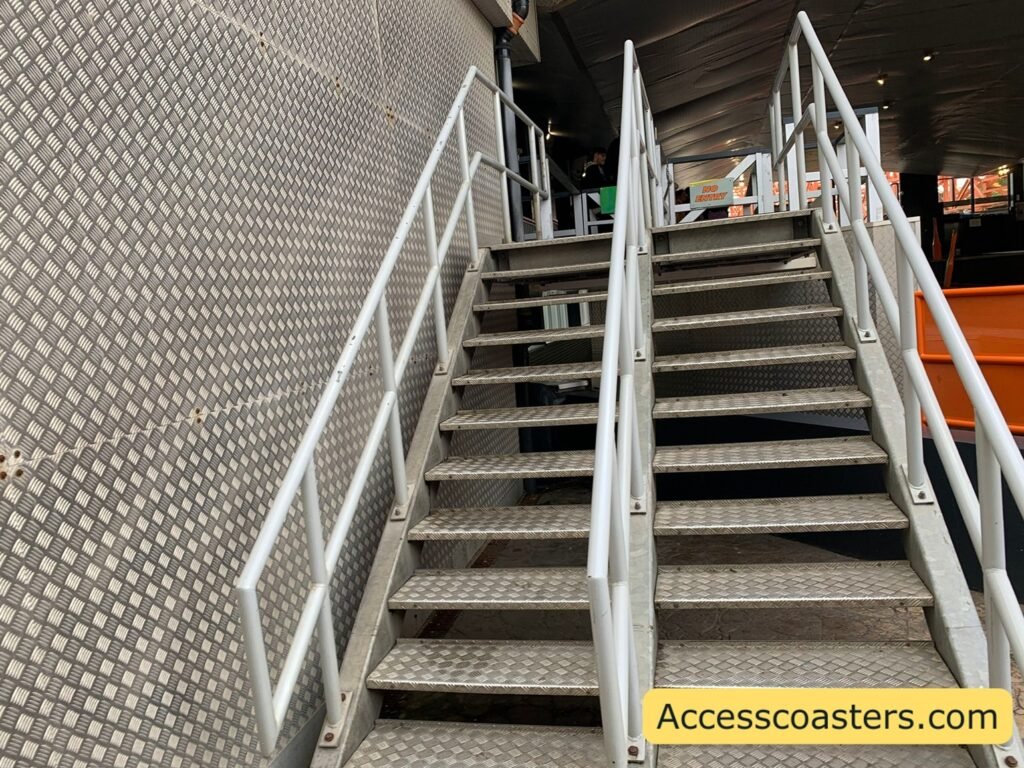 image shows 2 stair cases the left one is the eassy access and speedy pass entrance to the ride station for Nickelodeon Streak and the left is the exit stairs. both stair cases are metal stairs with double handrails and yellow painted edges. 