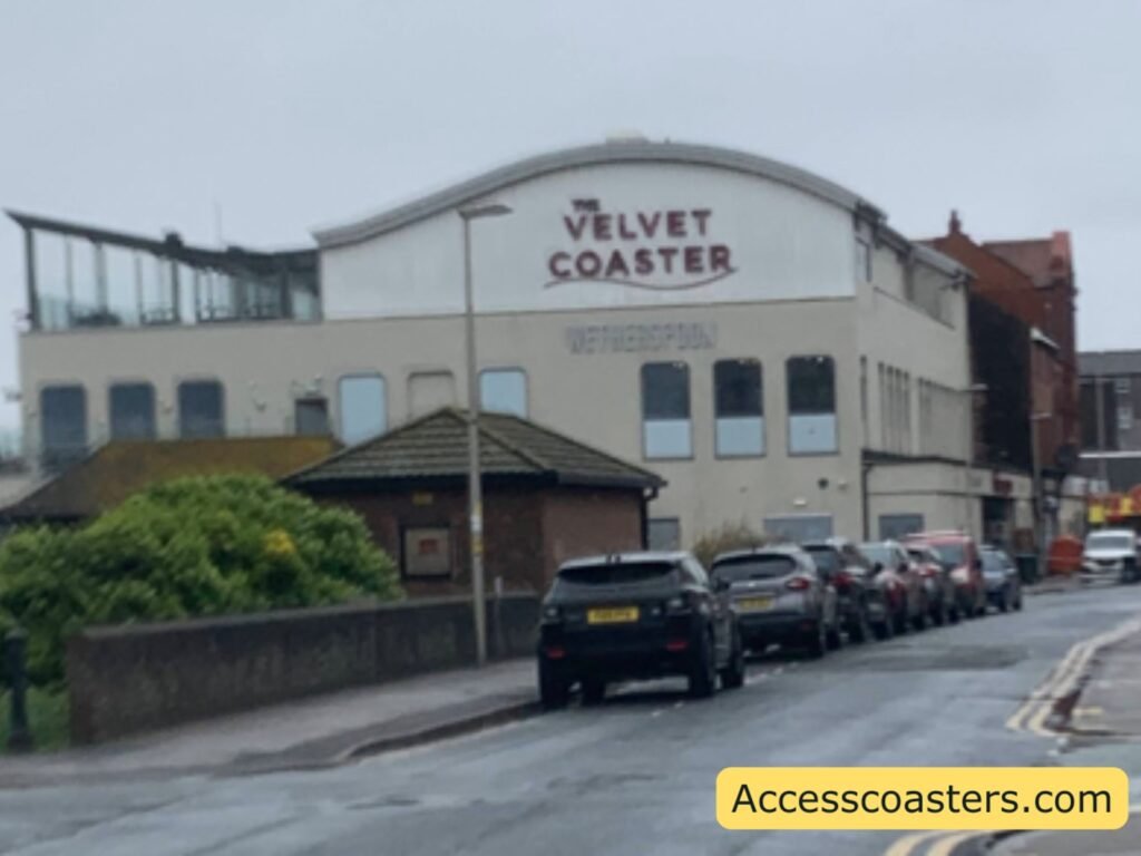 Street view of The Velvet Coaster Wetherspoons pub across from Pleasure Beach, with the large curved pub sign on the roof, cars parked along the road