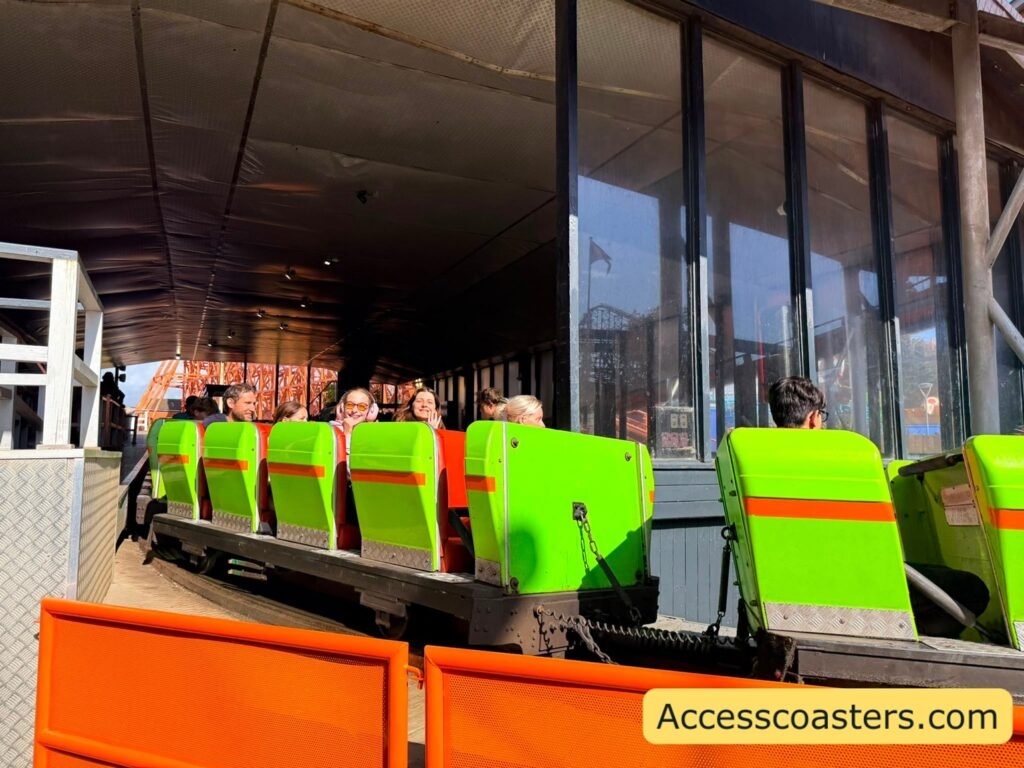 image shows Nickelodeon Streak train leaving the station and going around a bend part of the train is visible. with people smiling and enjoying the ride. 