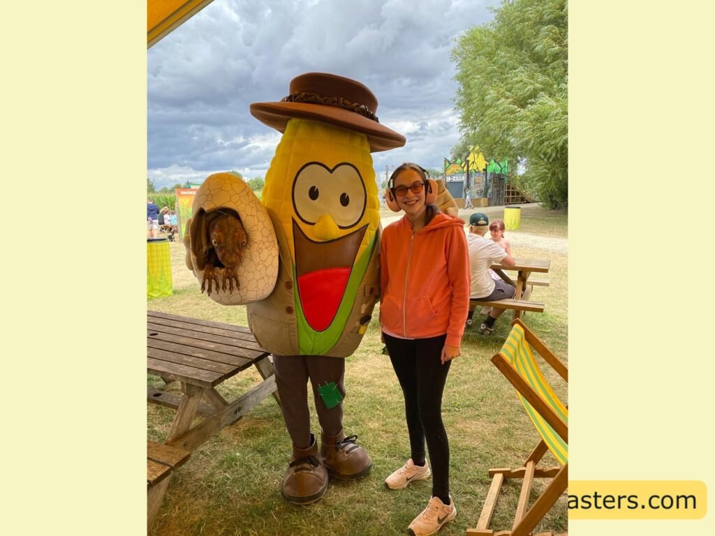 image of Iona stood next to Kernel Kernel who is dressed in a ranger outfit with brown coat, hat boots and holding a dinsour hatting out an egg in his hand. 