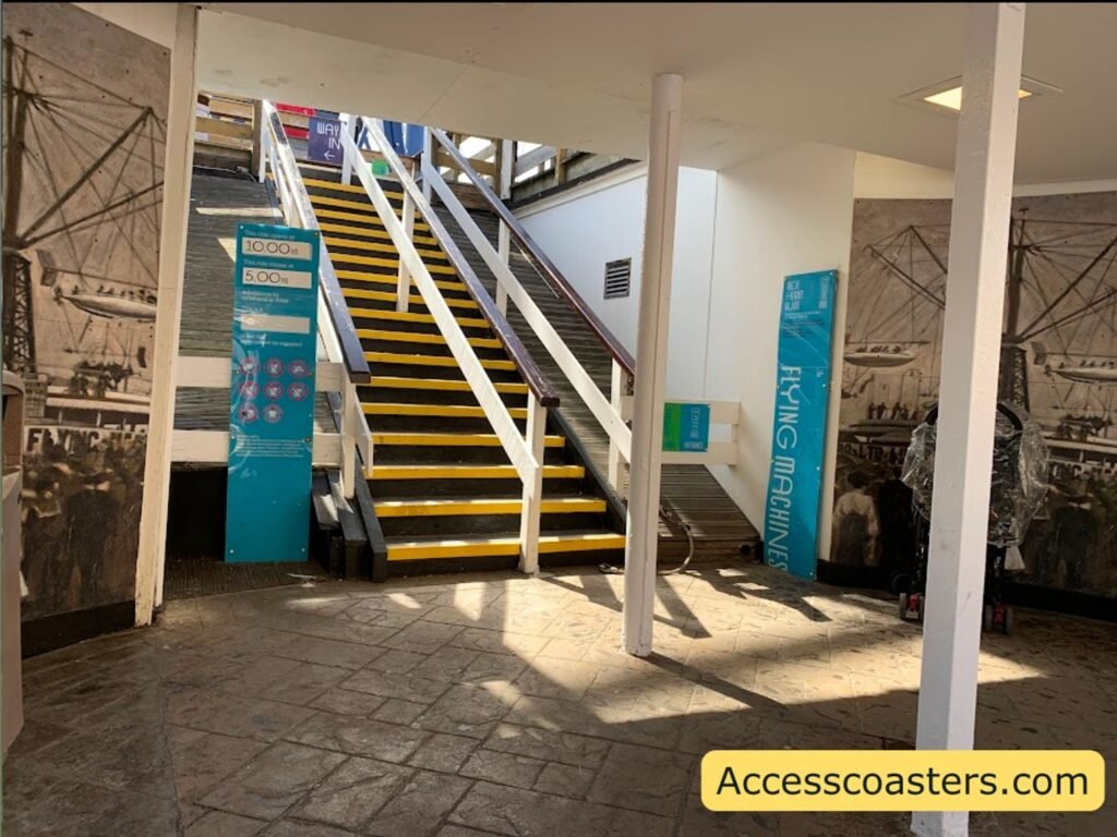 image of main entrance and easy access pass entrance for flying mashines Covered stairway  with yellow-edged steps and white walls leading to the Flying Machines ride station 
