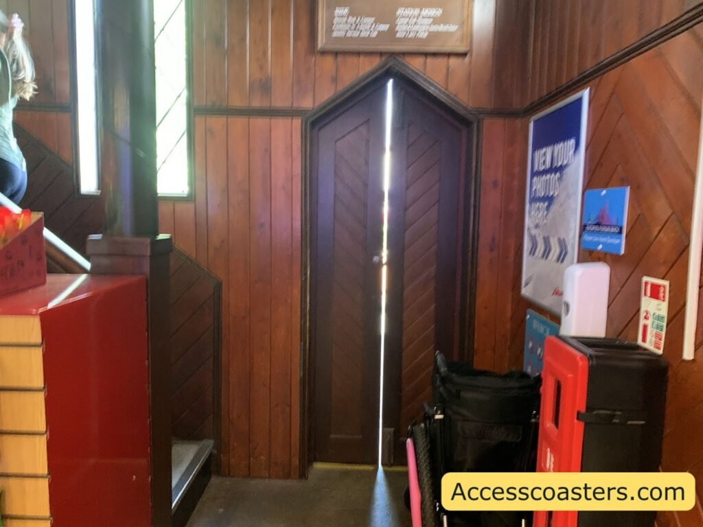 Interior view of the Avalanche easy access pass entrance inside the gift shop, showing a narrow wood‑panelled corridor with a pointed doorway and space to leave the wheelchair at bottem of staircase 