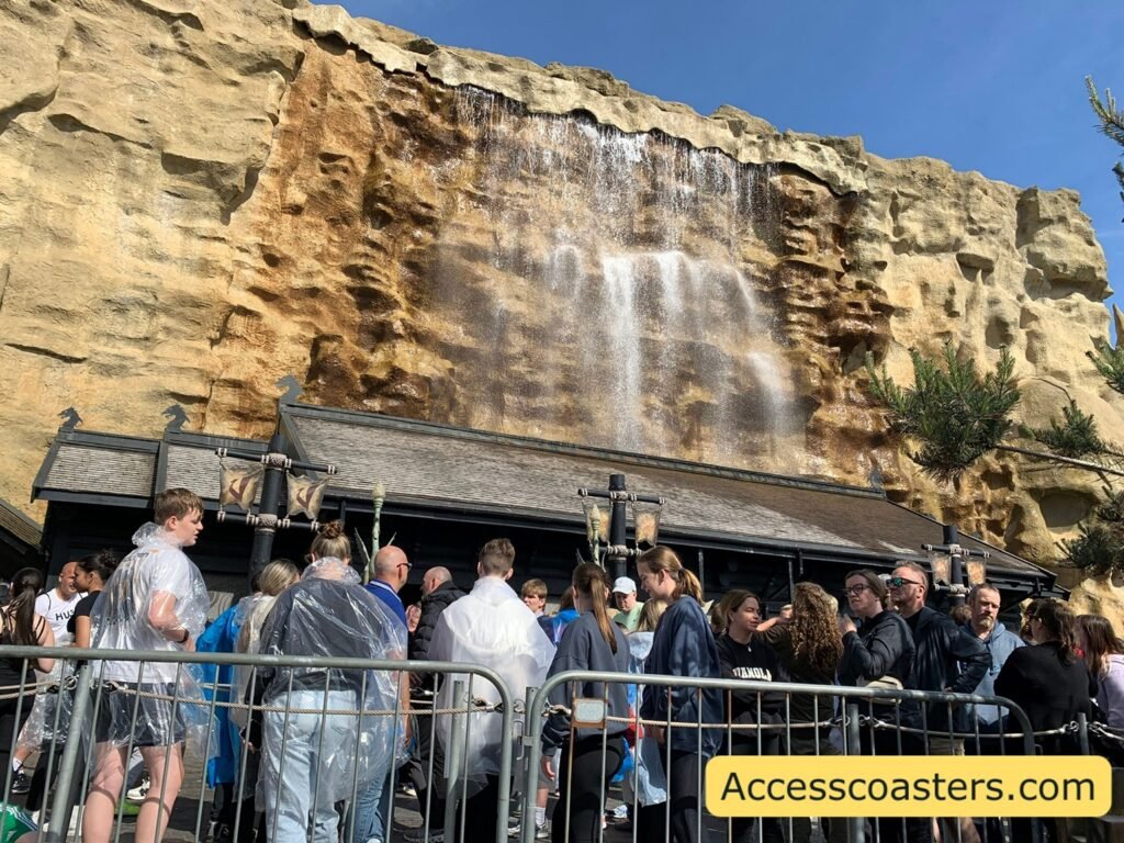 Guests waiting behind metal railings outside Valhalla, with the rocky façade and a large waterfall feature forming the backdrop of the queue area.
