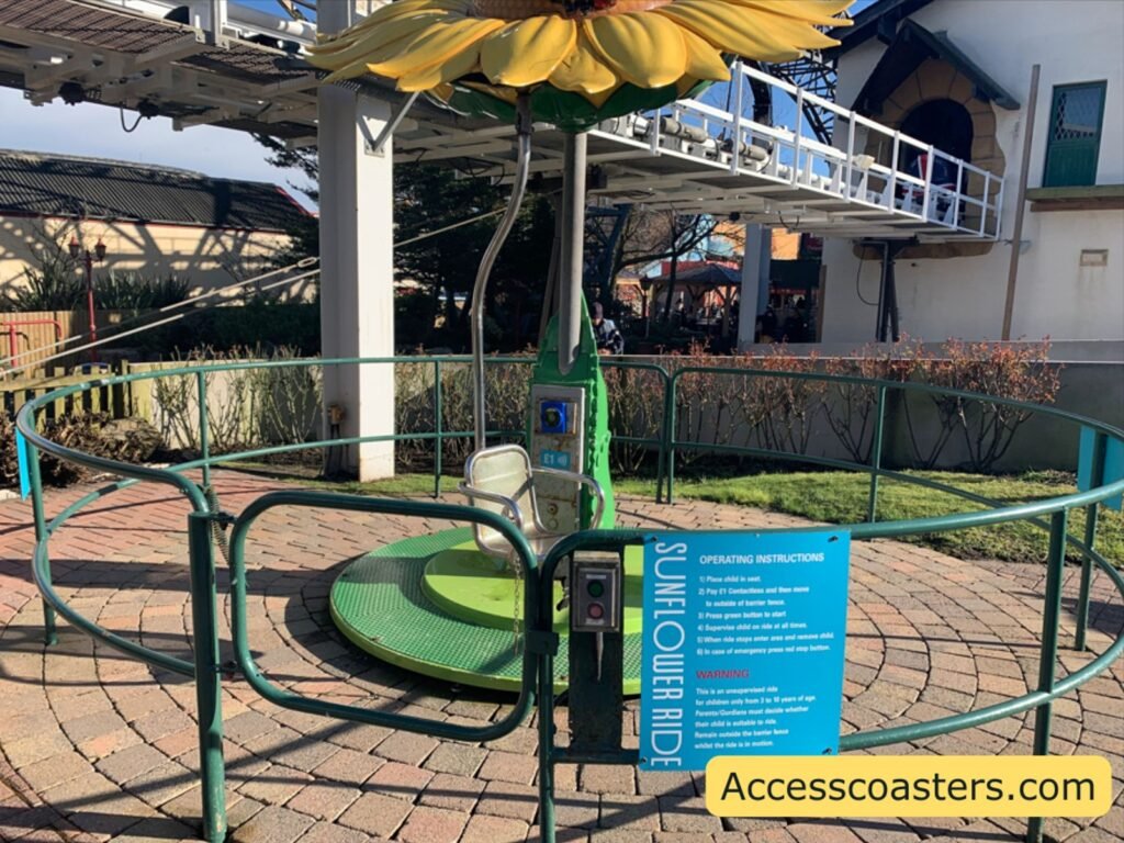  left: A round, green rotating play platform surrounded by metal railings, with a large sunflower-shaped canopy above it and a blue information sign on the railing. 