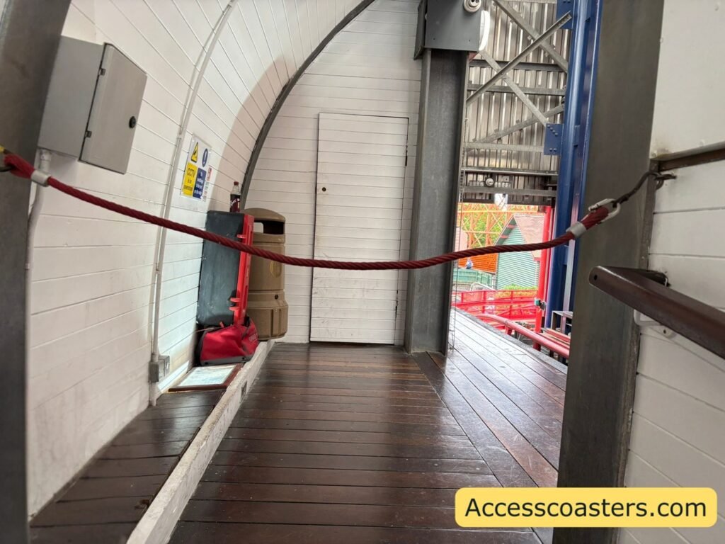 Indoor flat exit corridor with a red rope barrier and concrete walls, showing the step-free section of the ride exit