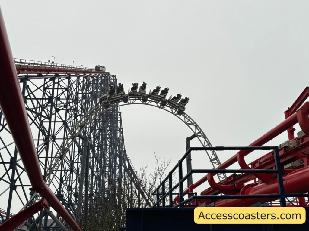 A large section of the ICON roller coaster track with a steep lift hill. A train full of riders is cresting the hill. 