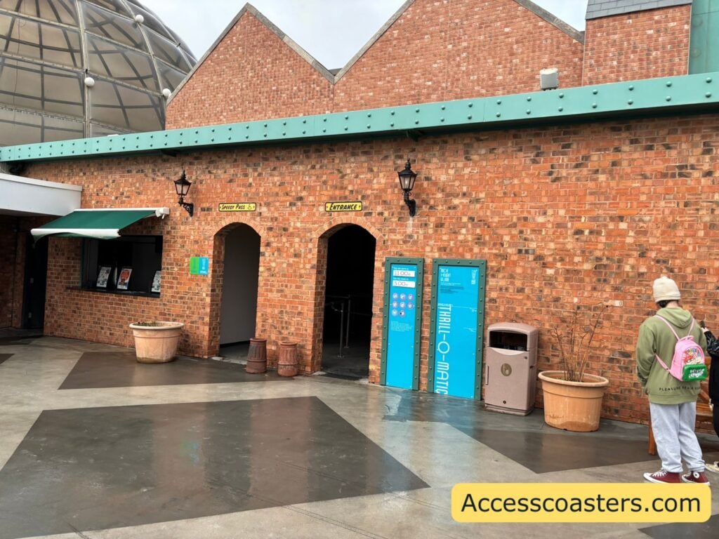 building with 2 arched doorways next to eachother the left door way has signs at the side that read easy access pass and speedy pass entrance as well as sign above the doorway that reads speedy pass with the wheelchair symbol next to it. the right doorway has a sign above that reads entrance and two ride restriction and information boards on the wall. 