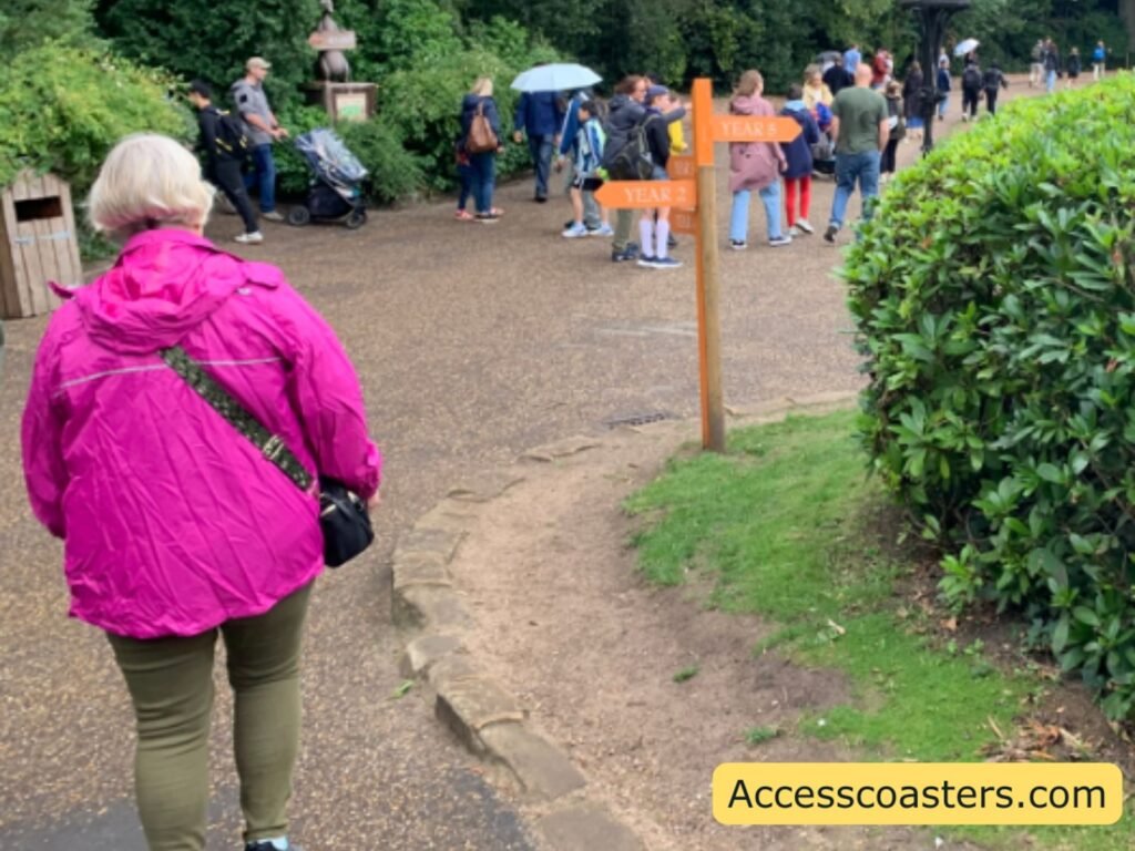 busy path with lots of people and an a orange sign with arrows coming off pointing to where each trail point is. 
