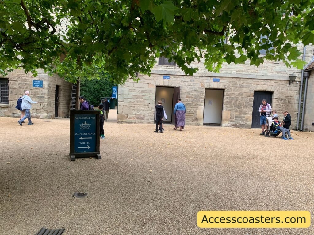 image if courtyard area with stone toilet block and a big stan up sign that reads welcome to warick castle main entrance with an arrow pointing left and toilets with an arrow pointing right 