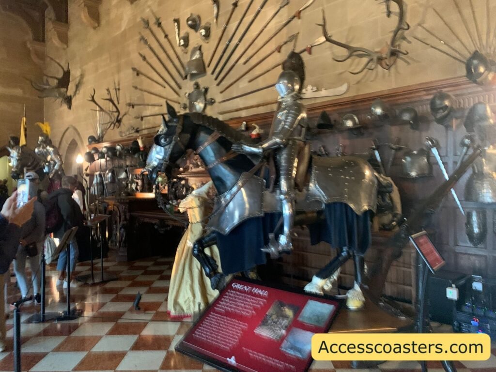 Great Hall armour display with a mounted armoured horse, full suits of armour, weapons fanned out on the wall, and wax figures in period dress standing among the 15th‑ and 16th‑century arms and armour collection.